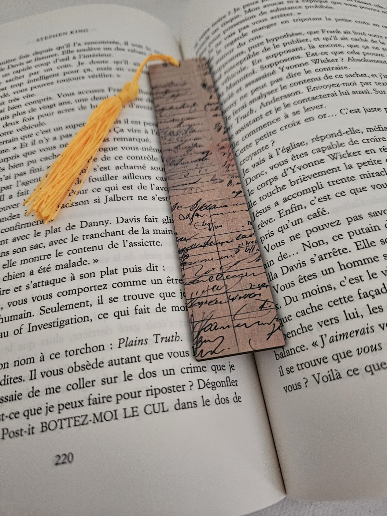 Marque page personnalisé avec un pompon jaune orangé qui représente des écritures très fine comme une ancienne lettre exposé sur un livre ouvert
