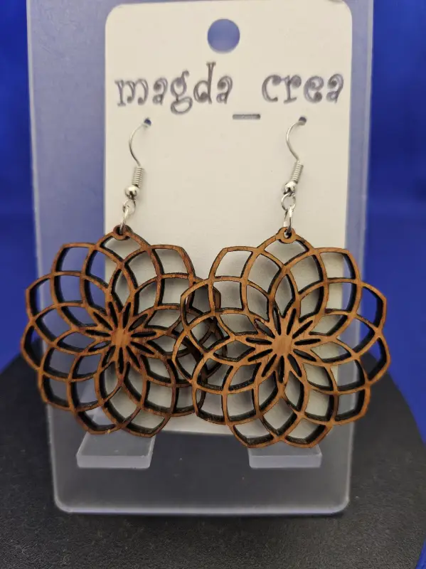 Paire de boucle d'oreilles en bois découpée au laser en forme de rosace. Attaché à des crochets couleur argent. Elle est mise en avant sur un présentoir transparent.