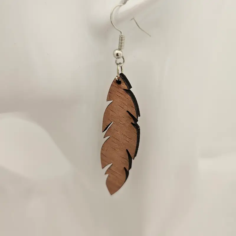 Paire de boucles d’oreilles en bois finement sculptées en forme de plume, présentées sur un élégant présentoir.