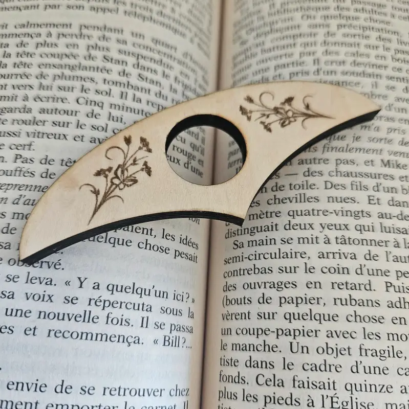 Bague de lecture bois découpé et gravé au laser posée sur un livreouvert avec des ornement